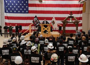 Secretary Marty Walsh stands in front of dozens of union workers wearing black shirts that read: stronger than ever.