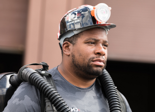 A male mine rescue worker wearing a hardhat and oxygen tank