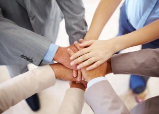 Group of colleagues dressed in various business casual attire joining hands in the middle to show unity.
