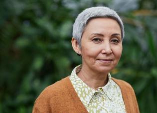 An older woman with short grey hair wearing a brown sweater and button down shirt.