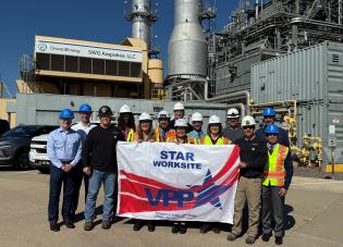 A group of people in hardhats stand in front of an energy plant holding a banner that says "STAR Worksite, VPP"