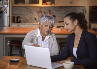 An older woman and her daughter look at retirement planning documents on a laptop.