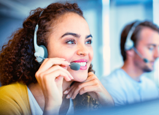 A woman wearing a headset smiles while working at a call center.