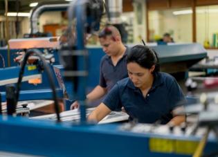 A woman with dark hair pulled back in a ponytail and wearing a blue uniform working in a factory.