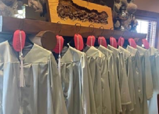 Graduation gowns hang in front of a fireplace.