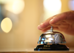 A hand ringing a bell on a hotel desk.