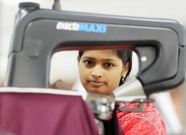 Uma jovem de Bangladesh vestindo roupa vermelha e sentada atrás de uma máquina de costura.