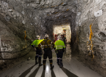 Three mine workers in an underground mine. All are wearing helmets and reflective gear.